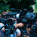 TV news cameras crowding together at an outdoor event