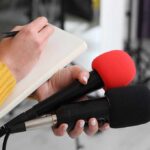 Journalist holding two microphones while writing in a notebook