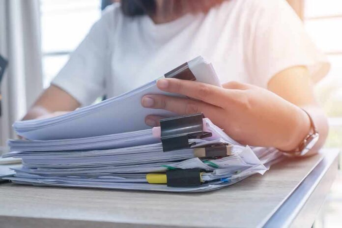 shutterstock_1122192059 Person organizing a stack of documents with binder clips