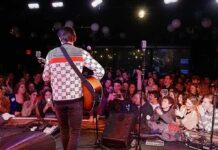 Guitarist performing on stage facing a cheering crowd