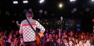 Guitarist performing on stage facing a cheering crowd