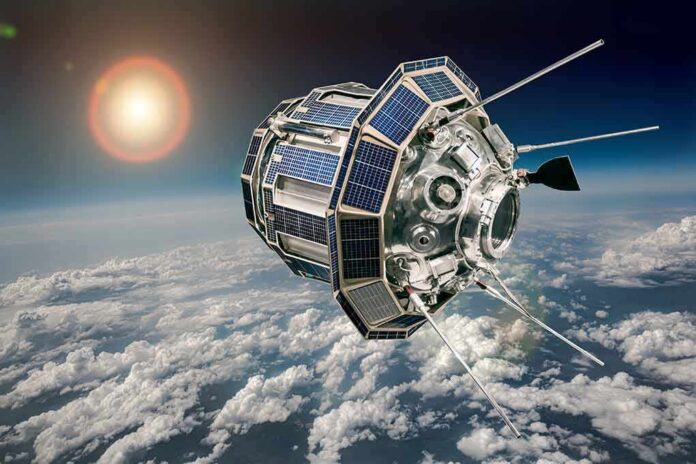 shutterstock_1493150903-1 Satellite with solar panels orbiting above Earth’s clouds