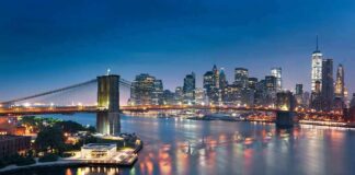 Brooklyn Bridge over river with illuminated city skyline at dusk