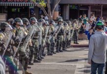 Stabbing Case Sparks ICE Detainer Fight Riot police in helmets and shields form a line on a city street