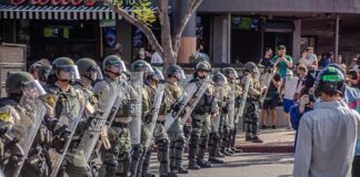 Stabbing Case Sparks ICE Detainer Fight Riot police in helmets and shields form a line on a city street