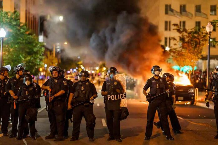 Christian Jones and Teddy Williams among police line at night protest with fire and smoke