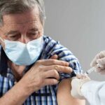 Older man in mask receiving a vaccine injection