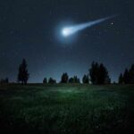Bright meteor streaking across a starry night sky over a grassy field