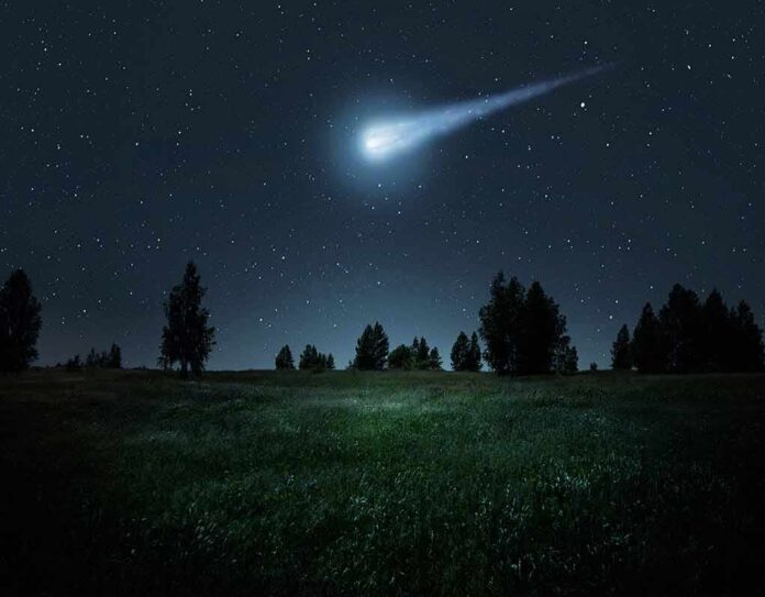 shutterstock_1898667577-1 Bright meteor streaking across a starry night sky over a grassy field