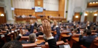 Legislators raise hands during a vote in a large chamber