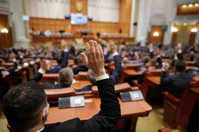 shutterstock_1919379416 Legislators raise hands during a vote in a large chamber