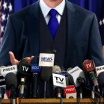 A speaker at a press conference with multiple microphones in front of them