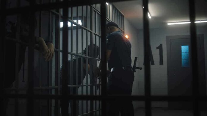 shutterstock_2438057445 police officer at a jail cell with detainees behind bars