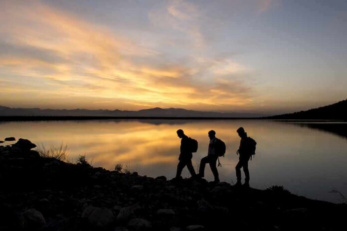 hikers silhouetted by a lake at sunset
