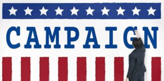 Trump-Aligned PAC Launches $10 Million Texas Ad Blitz Man in suit writing on large campaign banner with stars and stripes