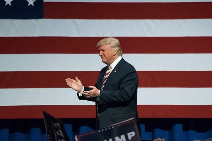 shutterstock_487546282 Donald Trump clapping on stage before a large American flag