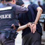 Police officer escorting a handcuffed man to a vehicle