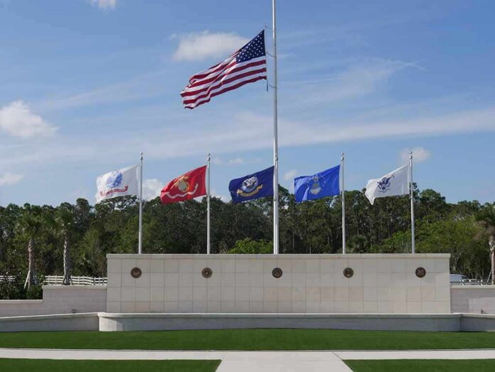 United States flag at half-mast above military branch flags at a memorial