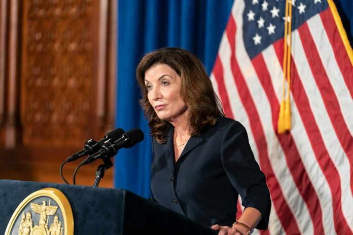 Kathy Hochul speaking at a podium with microphones and a U.S. flag behind her