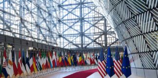 Row of national flags in a modern glass atrium with red carpet and EU and US flags upfront