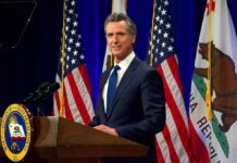 California Adds 1,000+ New Laws Man in suit speaking at a podium with American and California flags