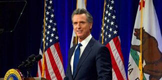 California Adds 1,000+ New Laws Man in suit speaking at a podium with American and California flags