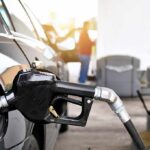 Gas pump nozzle fueling a black car at a station