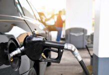 Gas pump nozzle fueling a black car at a station
