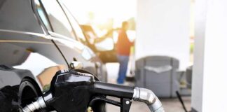Gas pump nozzle fueling a black car at a station
