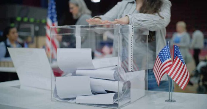 shutterstock_2454758129 Person casting a ballot into a clear box at a polling station