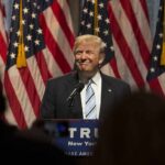 Man in suit speaking at podium with American flags behind