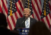 Man in suit speaking at podium with American flags behind