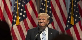 Man in suit speaking at podium with American flags behind