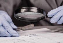 Gloved hands examine bullet casing with magnifying glass