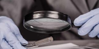 Gloved hands examine bullet casing with magnifying glass