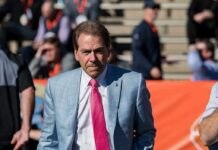 Trump Plans Alabama-Georgia Game Appearance Nick Saban in a light blue plaid suit with a pink tie at a football stadium; Chuck Howley not visible