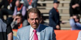 Nick Saban in a light blue plaid suit with a pink tie at a football stadium; Chuck Howley not visible