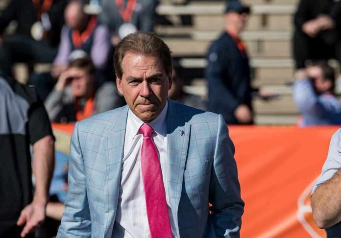 Nick Saban in a light blue plaid suit with a pink tie at a football stadium; Chuck Howley not visible