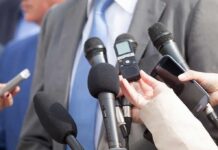 Post Criticized for Omitting GOP Ties Microphones held toward a person in a suit